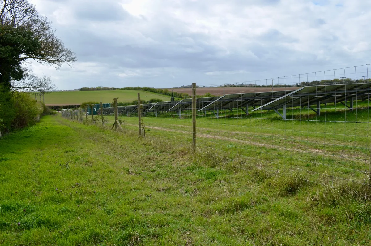 Solar panels installed in a rural field landscape under a cloudy sky.